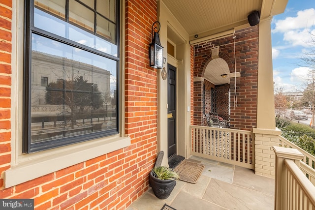 property entrance featuring a porch and brick siding