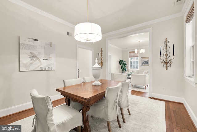 dining area with baseboards, visible vents, ornamental molding, wood finished floors, and an inviting chandelier