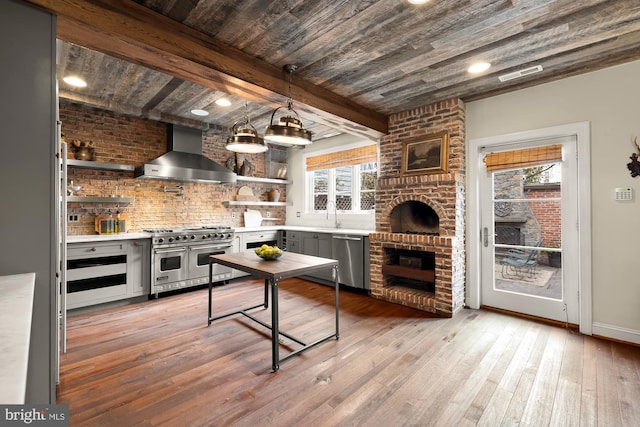 kitchen featuring open shelves, appliances with stainless steel finishes, wall chimney range hood, and light countertops