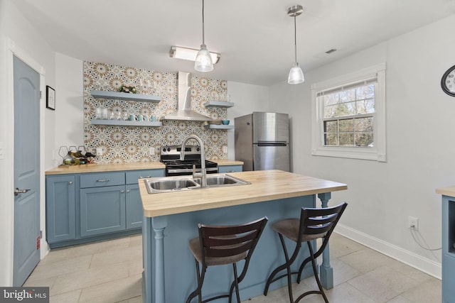 kitchen with blue cabinets, butcher block counters, appliances with stainless steel finishes, wall chimney exhaust hood, and open shelves