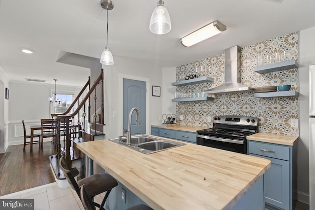 kitchen featuring open shelves, wall chimney range hood, blue cabinetry, and stainless steel range with electric stovetop