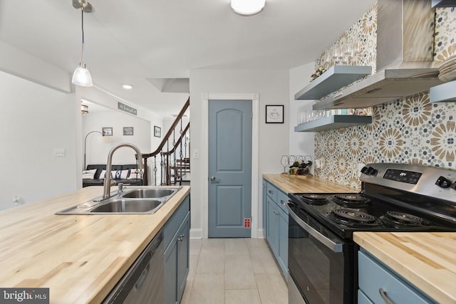 kitchen with appliances with stainless steel finishes, butcher block countertops, wall chimney range hood, and decorative light fixtures