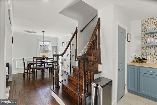 stairs featuring a chandelier, visible vents, crown molding, and wood finished floors