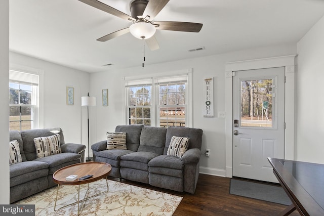 living area featuring a ceiling fan, visible vents, dark wood finished floors, and baseboards