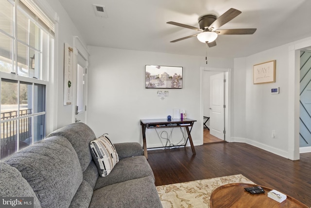 living room with dark wood-type flooring, visible vents, baseboards, and a ceiling fan