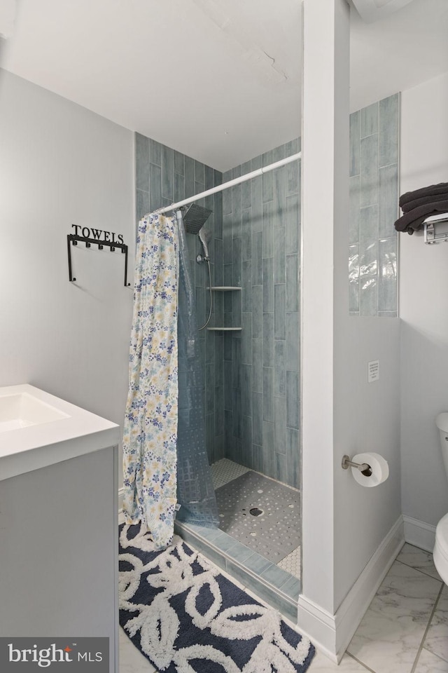 bathroom with marble finish floor, toilet, a stall shower, a sink, and baseboards