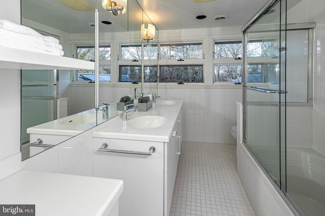 full bathroom featuring tile patterned flooring, toilet, shower / bath combination with glass door, tile walls, and vanity