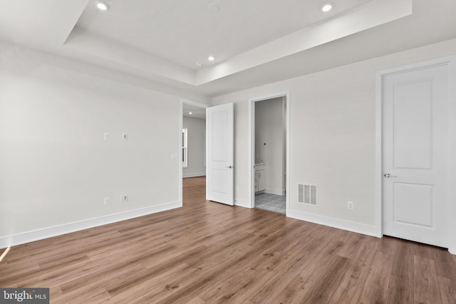 unfurnished bedroom with a tray ceiling, connected bathroom, and wood-type flooring