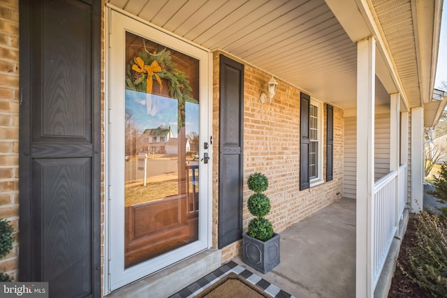 doorway to property with a porch and brick siding