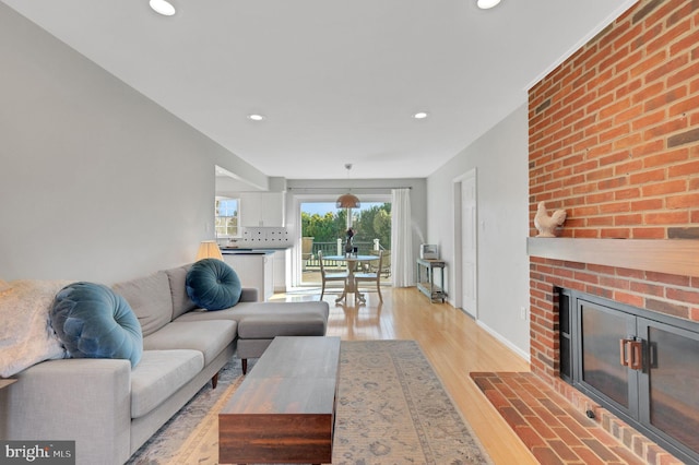 living room with recessed lighting, a brick fireplace, and light wood finished floors