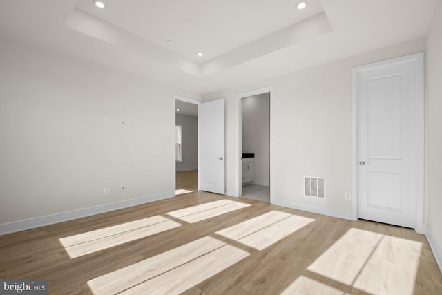 unfurnished bedroom featuring a tray ceiling, connected bathroom, and hardwood / wood-style flooring