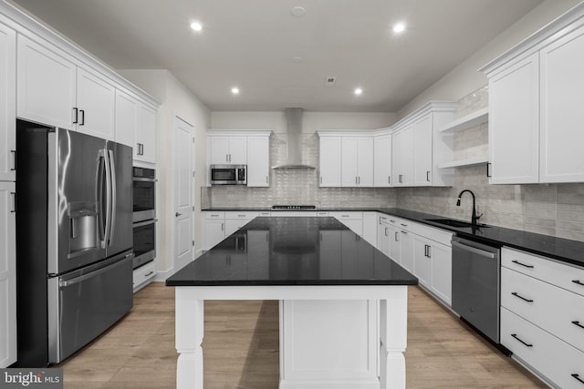 kitchen featuring appliances with stainless steel finishes, wall chimney exhaust hood, white cabinets, a center island, and sink