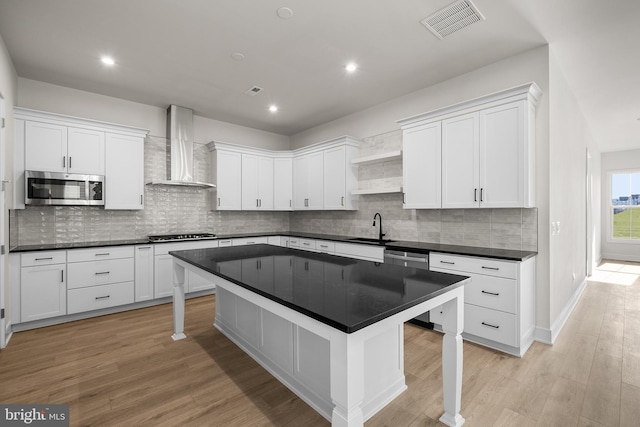 kitchen with white cabinets, wall chimney range hood, a kitchen bar, and stainless steel appliances