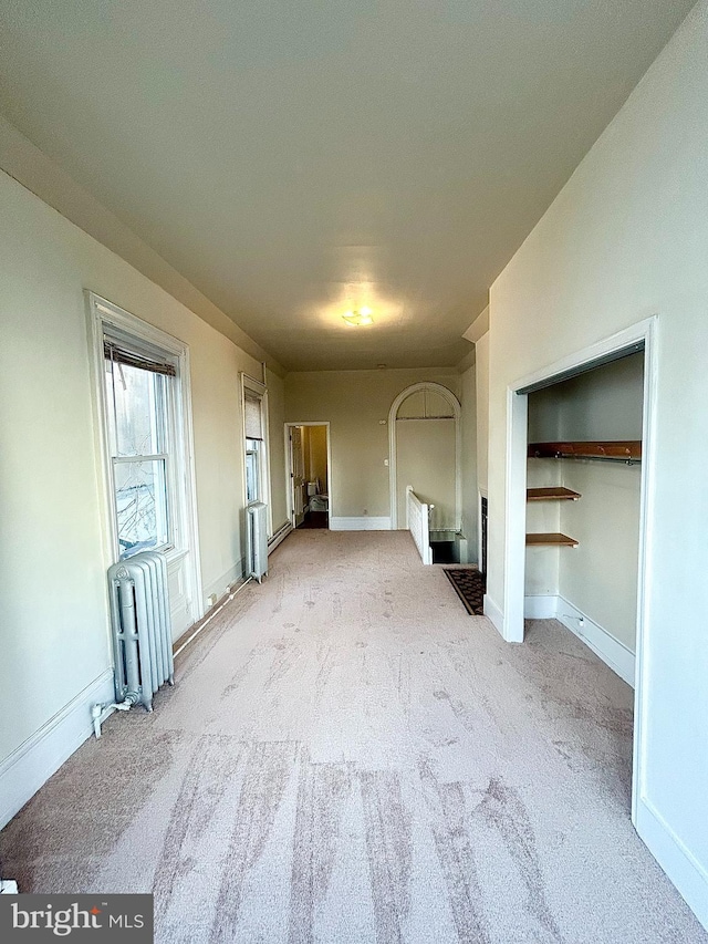 unfurnished bedroom with radiator, light carpet, and baseboards