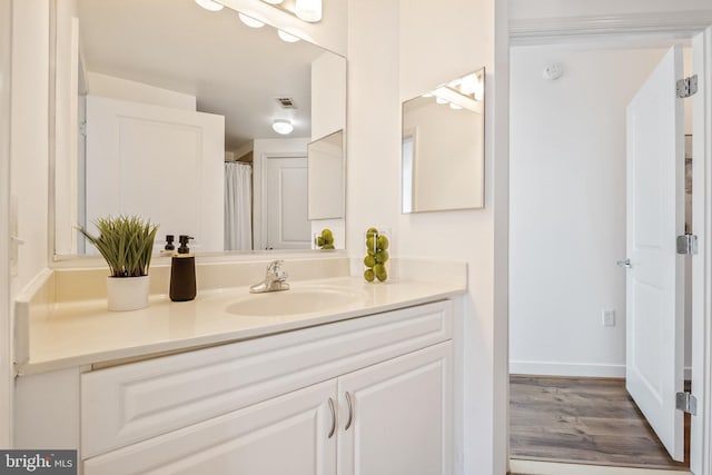 full bath featuring visible vents, vanity, baseboards, and wood finished floors