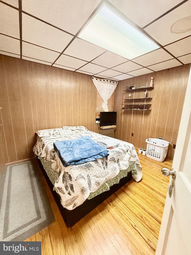 bedroom with hardwood / wood-style floors, a paneled ceiling, and wood walls