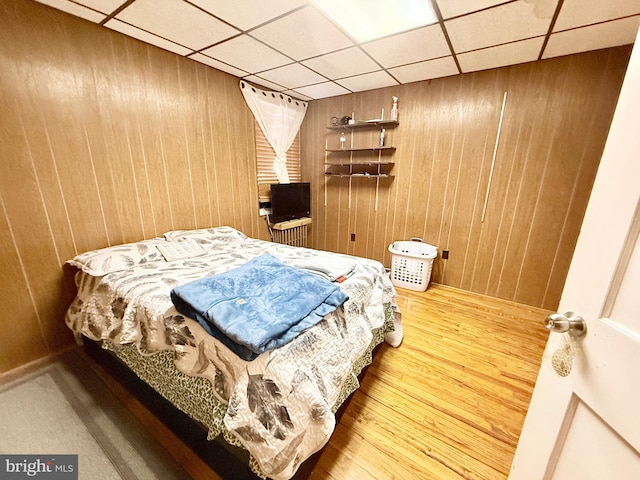 bedroom with hardwood / wood-style floors, a paneled ceiling, and wood walls