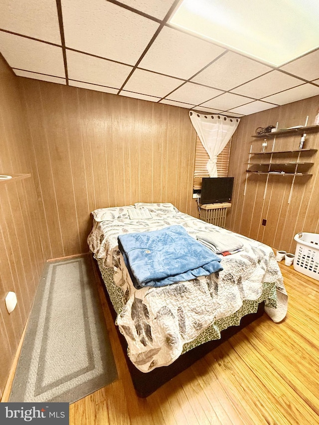 bedroom with hardwood / wood-style flooring, a paneled ceiling, and wooden walls