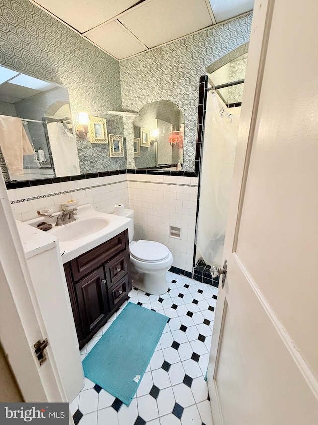 bathroom featuring tile walls, toilet, vanity, and curtained shower