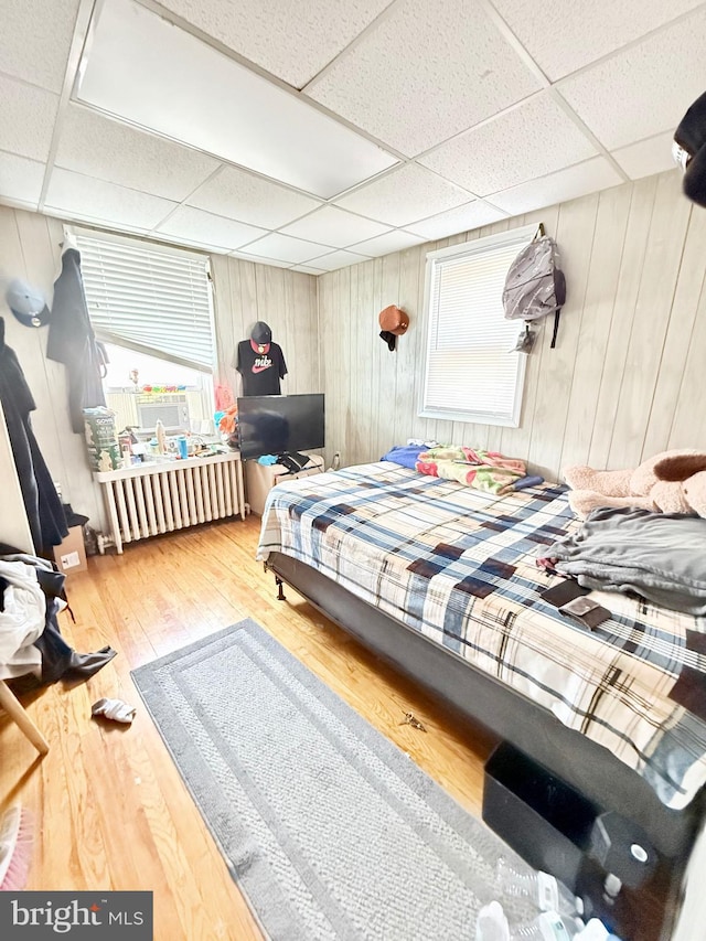 bedroom with a paneled ceiling, hardwood / wood-style floors, and radiator heating unit