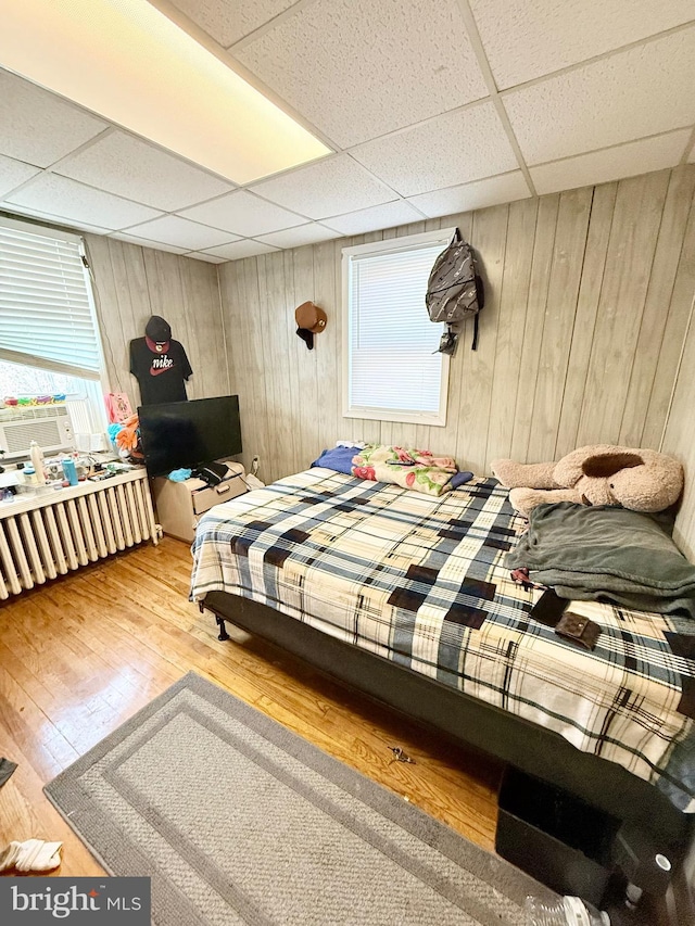 bedroom featuring a paneled ceiling, hardwood / wood-style floors, cooling unit, and wooden walls