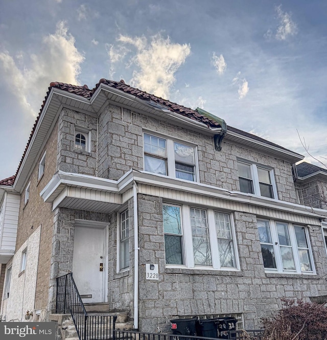 view of front of home featuring entry steps, stone siding, and a tile roof