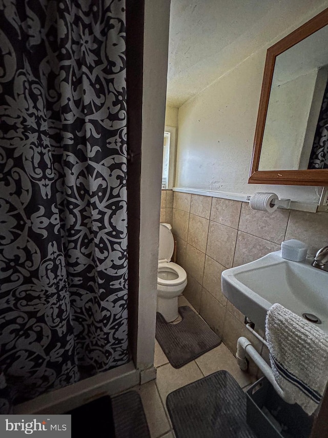 bathroom with toilet, a sink, tile walls, tile patterned floors, and walk in shower