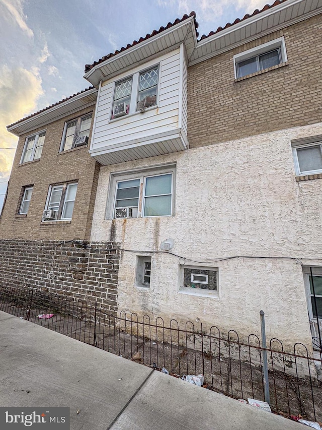 view of side of property with a tile roof, fence, and stucco siding