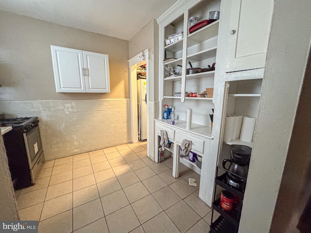 kitchen featuring light tile patterned floors, white cabinets, wainscoting, stainless steel gas stove, and open shelves