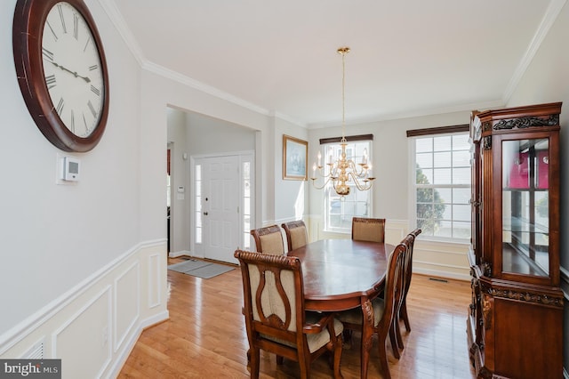 dining room with a notable chandelier, a decorative wall, ornamental molding, wainscoting, and light wood-type flooring