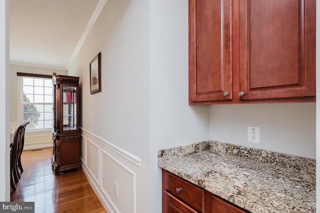 interior space with ornamental molding, wainscoting, a decorative wall, and wood finished floors