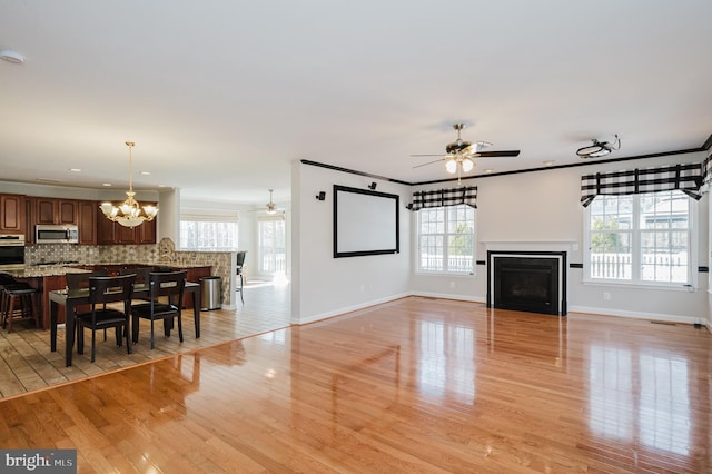 living area featuring light wood-style floors, a fireplace, crown molding, and ceiling fan with notable chandelier