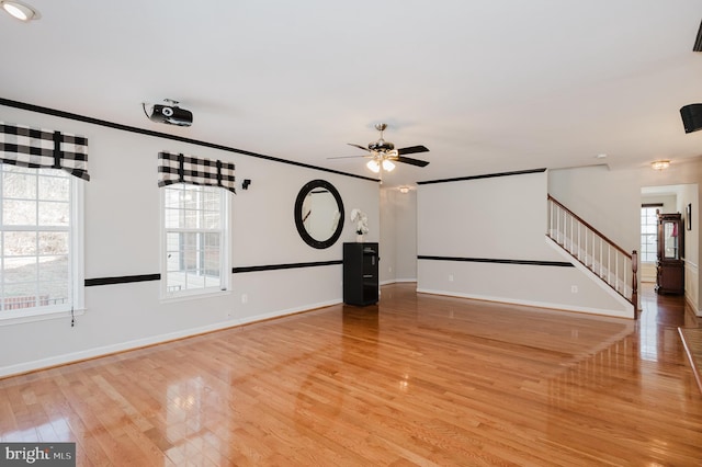 unfurnished living room featuring light wood-style flooring, stairway, baseboards, and ornamental molding