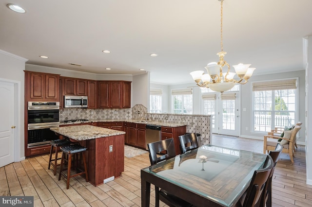 kitchen with a center island, pendant lighting, tasteful backsplash, appliances with stainless steel finishes, and light wood-style floors