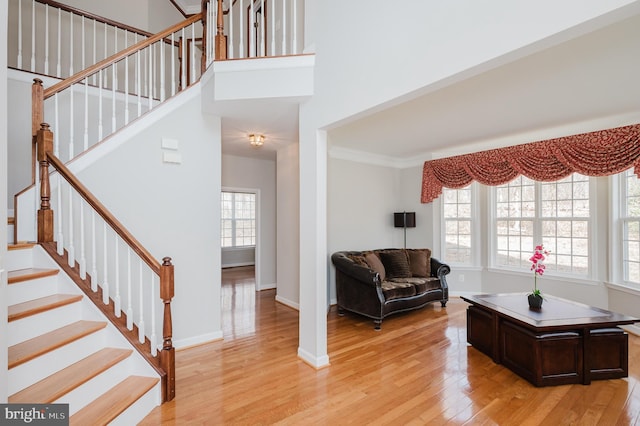 entryway featuring light wood finished floors, baseboards, a towering ceiling, ornamental molding, and stairs