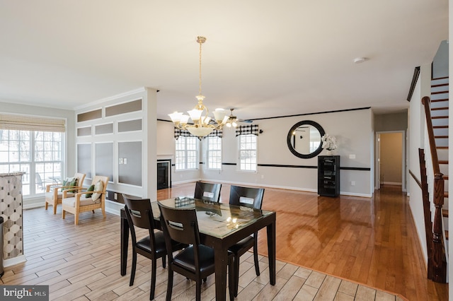 dining room with light wood-style floors, a wealth of natural light, an inviting chandelier, and stairs