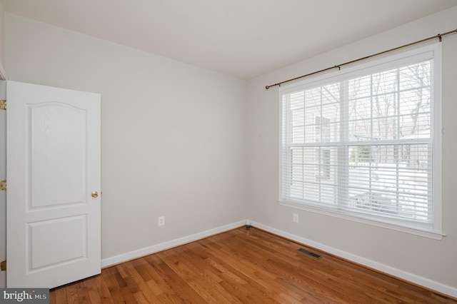 empty room with a healthy amount of sunlight, baseboards, visible vents, and wood finished floors