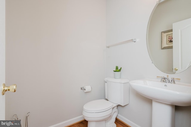 half bathroom with baseboards, a sink, toilet, and wood finished floors