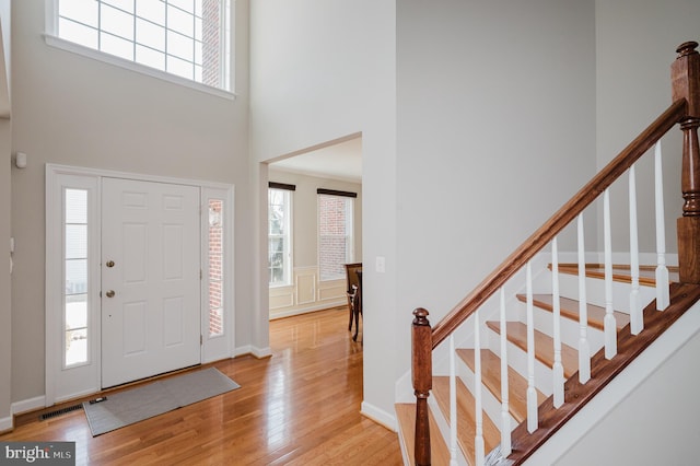 entrance foyer with baseboards, visible vents, a towering ceiling, stairway, and light wood-style floors