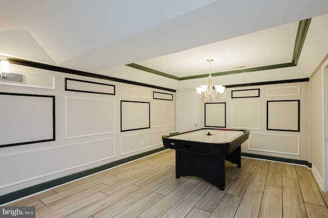 recreation room with a decorative wall, vaulted ceiling, ornamental molding, wood tiled floor, and an inviting chandelier