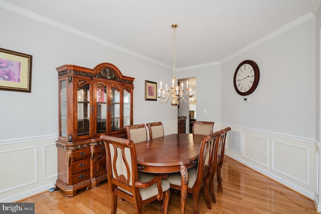 dining room with light wood-type flooring, a wainscoted wall, and a chandelier