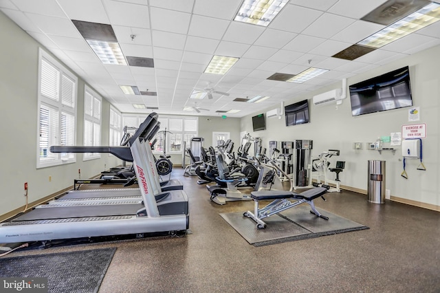 workout area with a wall unit AC, a paneled ceiling, and baseboards