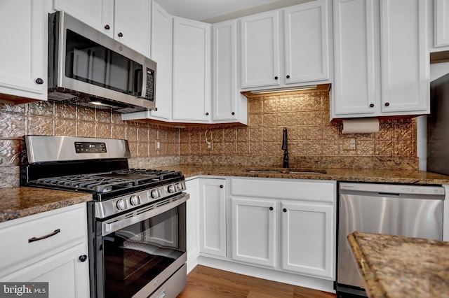 kitchen with white cabinets, dark stone countertops, stainless steel appliances, and a sink