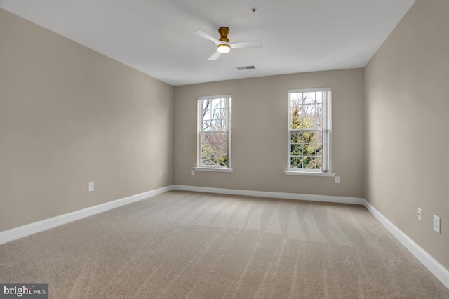 carpeted empty room featuring a healthy amount of sunlight, visible vents, ceiling fan, and baseboards