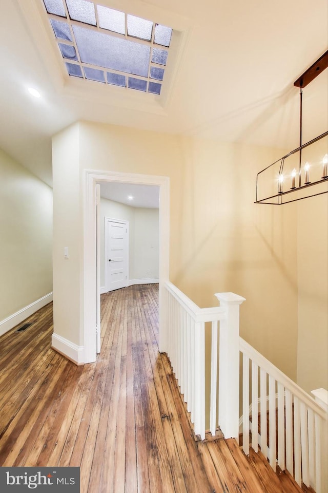 hallway with baseboards, a notable chandelier, hardwood / wood-style floors, and an upstairs landing