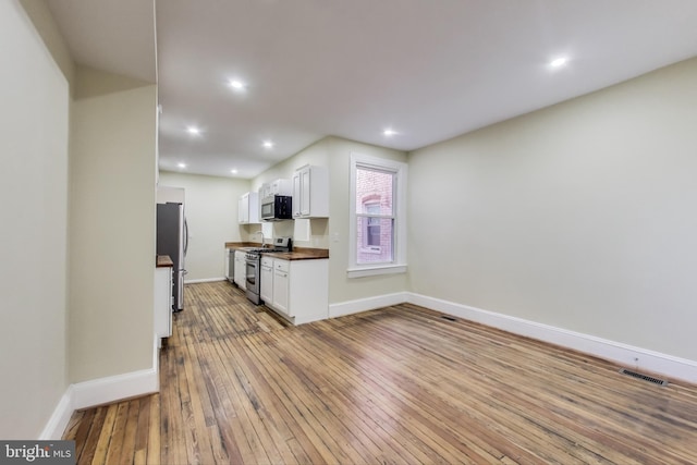 kitchen featuring light wood-style flooring, stainless steel appliances, visible vents, white cabinetry, and dark countertops