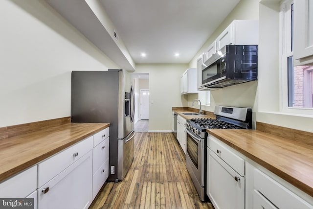 kitchen with stainless steel appliances, butcher block counters, white cabinets, and a sink