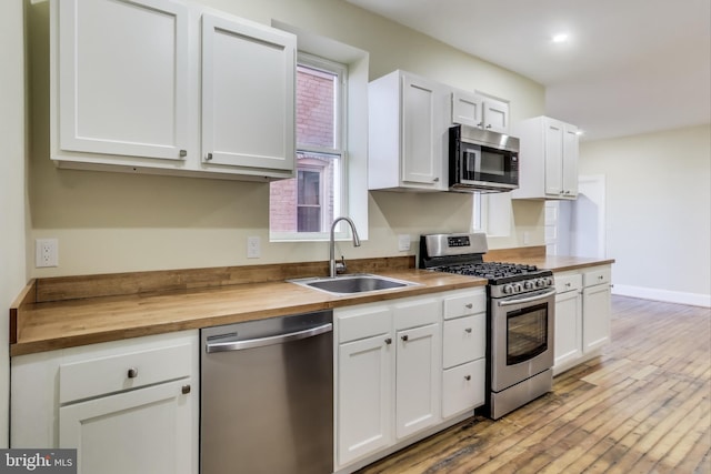 kitchen with light wood-style flooring, appliances with stainless steel finishes, white cabinetry, a sink, and butcher block countertops