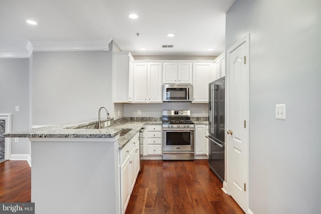 kitchen with appliances with stainless steel finishes, white cabinetry, a sink, light stone countertops, and a peninsula