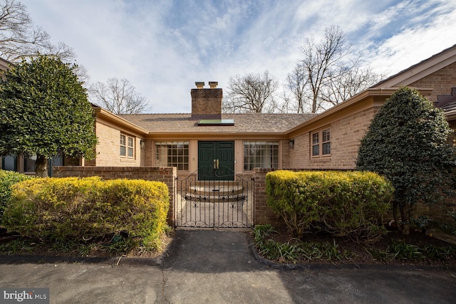 ranch-style home featuring a gate, brick siding, fence, and a chimney